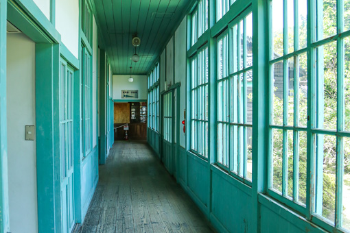 Inside a hallway in the Awashima Maritime Museum. The hallway is wooden with white walls and trim painted the same teal as the outside of the building. Many doors and windows line the hallway on either side.