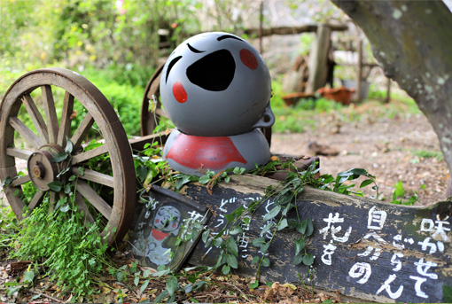 A statue made of 2 buoys to look like a jizo statue. Japanese text decorates a wooden plank below the statue.